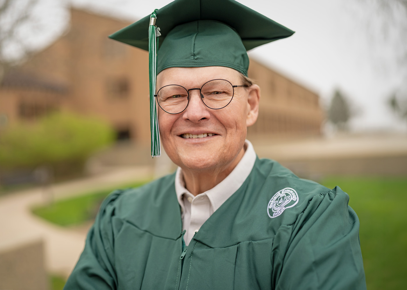 Don Fenton posing outdoors on campus. It's a close up photo and he's wearing his green o c c graduation cap and gown