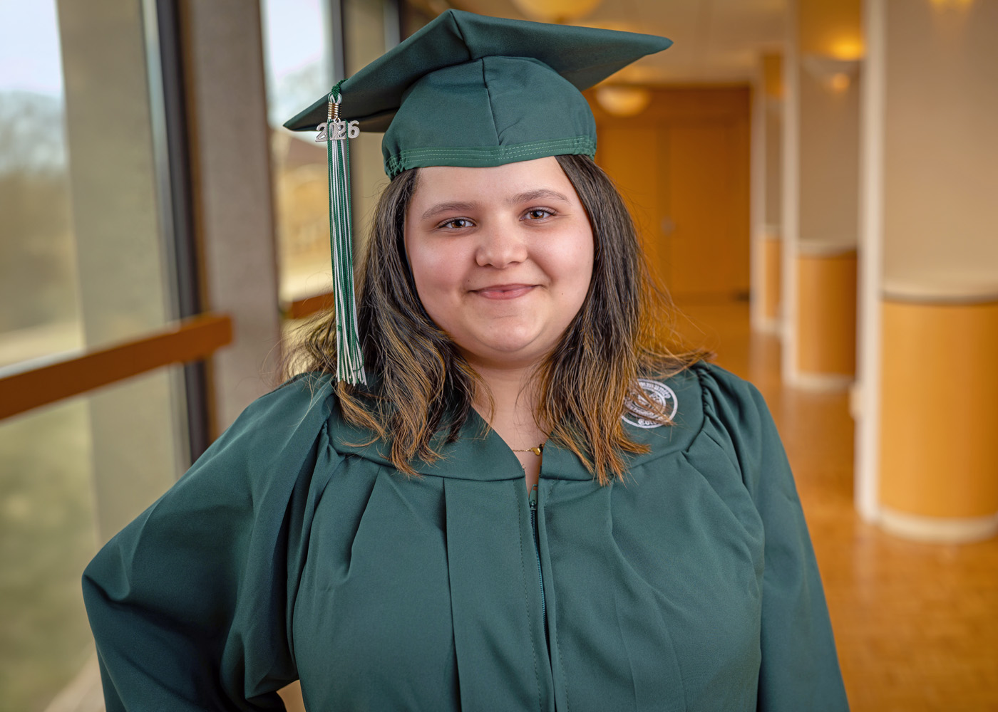 Lizelle Hees posing indoors on campus in her green O C C graduation cap and gown