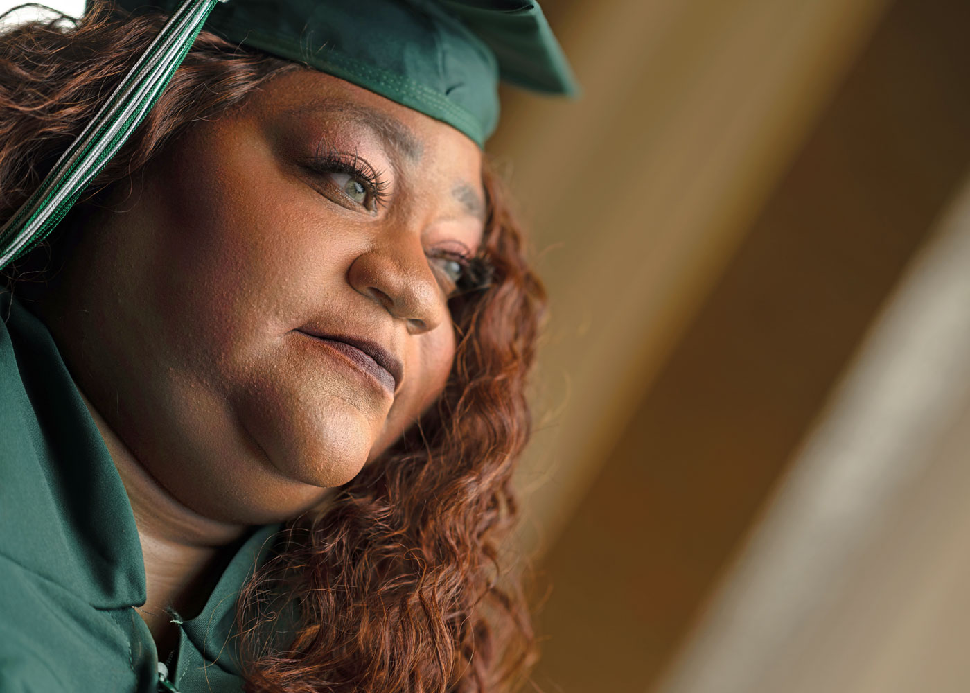 Close up of Ebony Boatman's face looking up and towards the side of her face. She's wearing her green O C C graduation cap and gown
