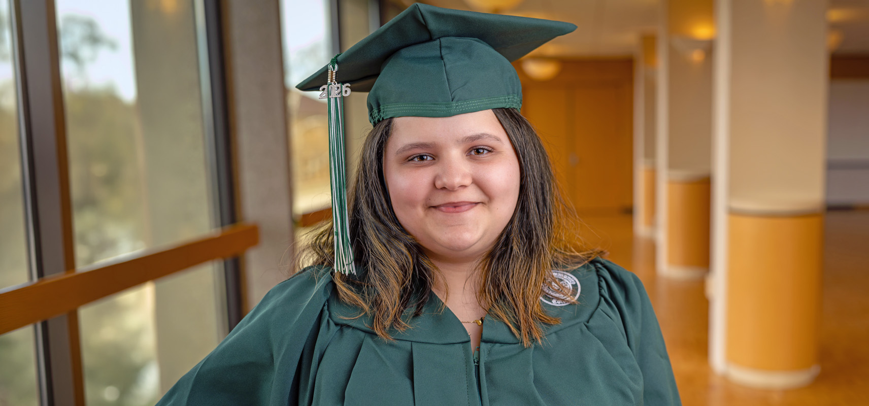 Lizelle Hees posing indoors on campus wearing her green O C C graduation cap and gown