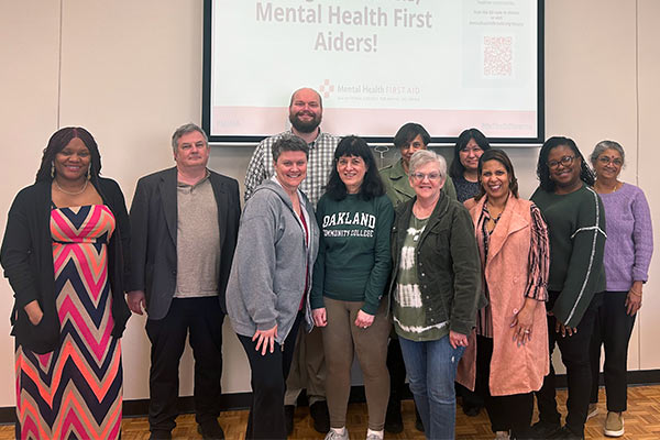 Group of employees standing in front of a projection screen that states “Mental Health First Aiders.”