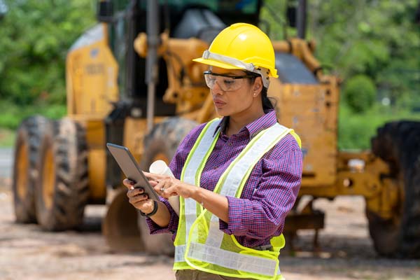 Image of a woman in a hardhat at a construction site on a tablet. 