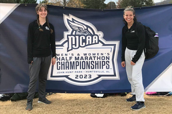 Two student athletes stand in front of NJCAA Half Marathon Championships sign
