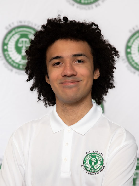 Blasé Johnson Portrait of a young man in a white polo shirt with a green logo, standing in front of a branded backdrop.