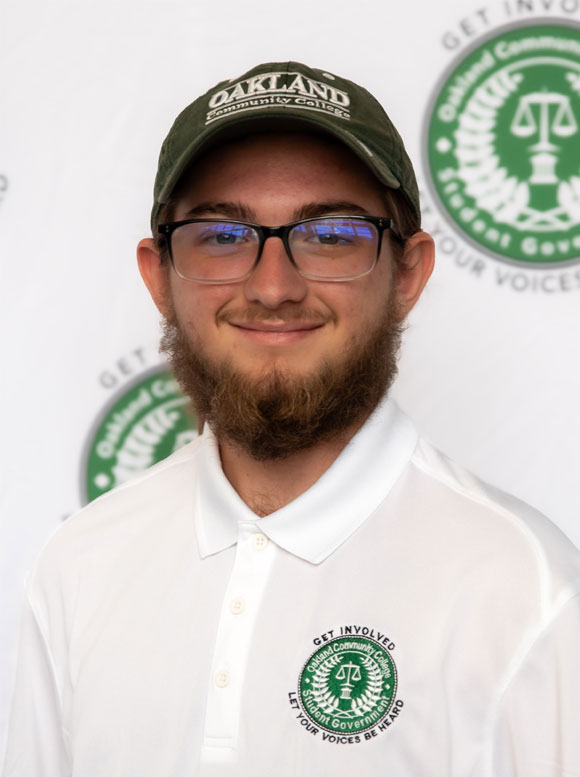 Jackson Jankowski Portrait of a man wearing an Oakland Community College cap and a white Get Involved Student Government polo shirt
