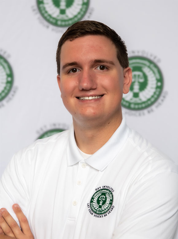 Robert Pawlowski Portrait of a man in a white polo shirt before a backdrop with repeated green circular logos.